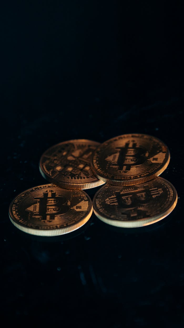 Four gold-colored Bitcoin coins arranged on a dark surface.